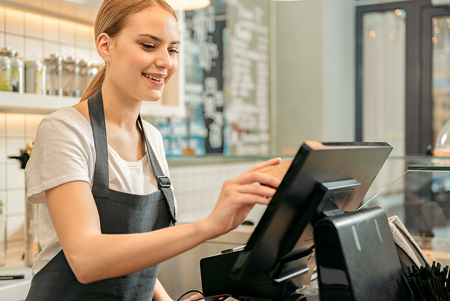 Joyful young saleswoman is receiving money from customer. She is holding credit card near screen and smiling